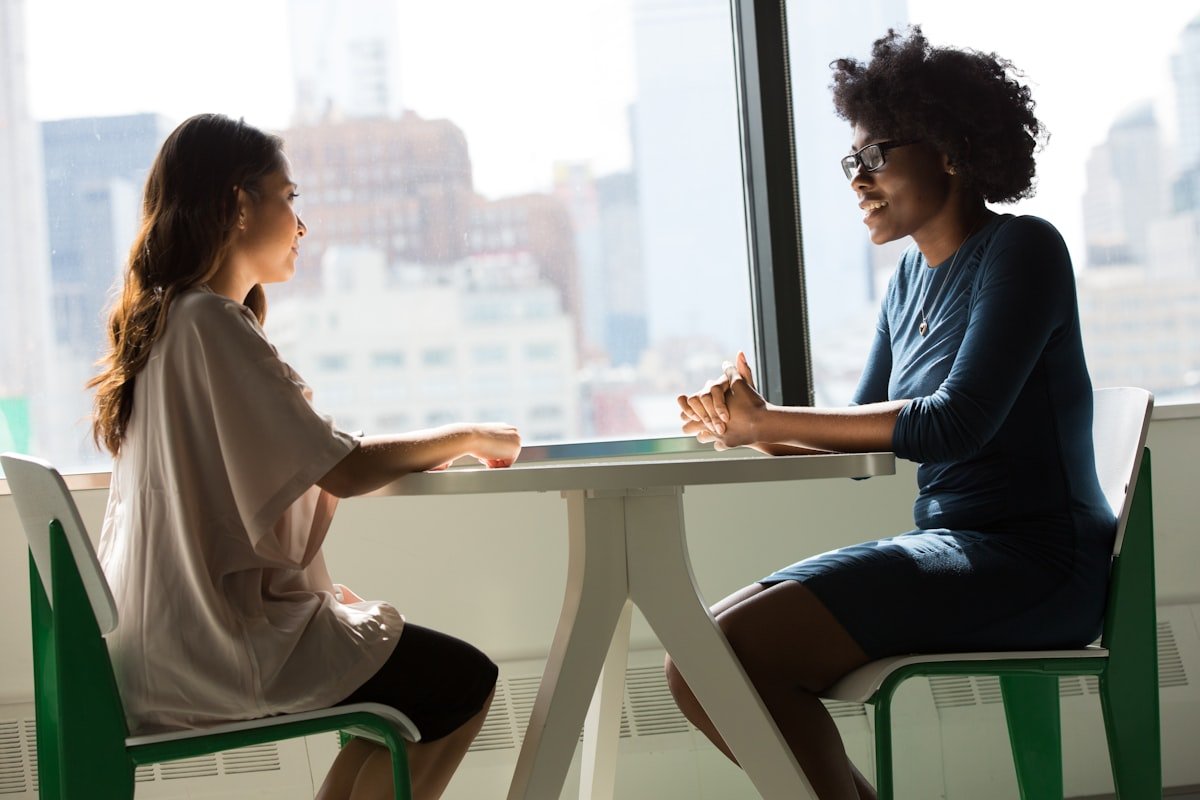 Two women in a focused one-to-one conversation by a bright window