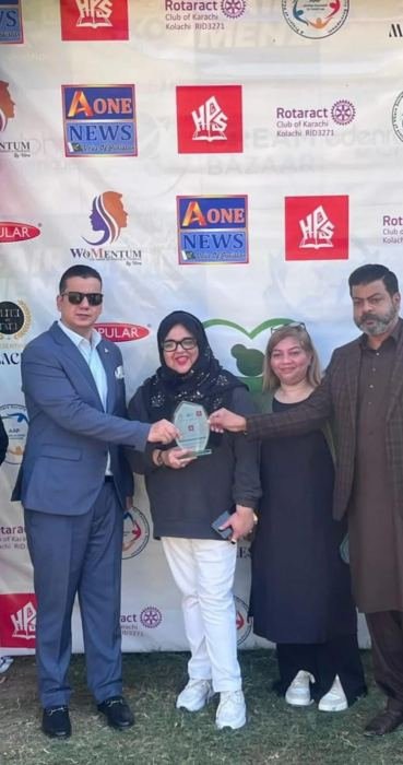 A glass shield being presented in front of a sponsor backdrop at an outdoor community event
