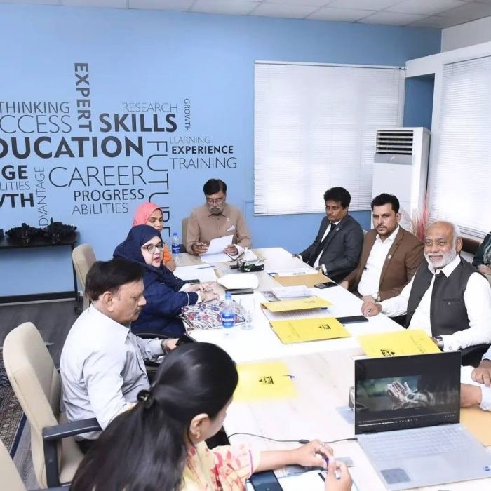 A working meeting around a table in a room with a wall graphic reading education, skills, career and training