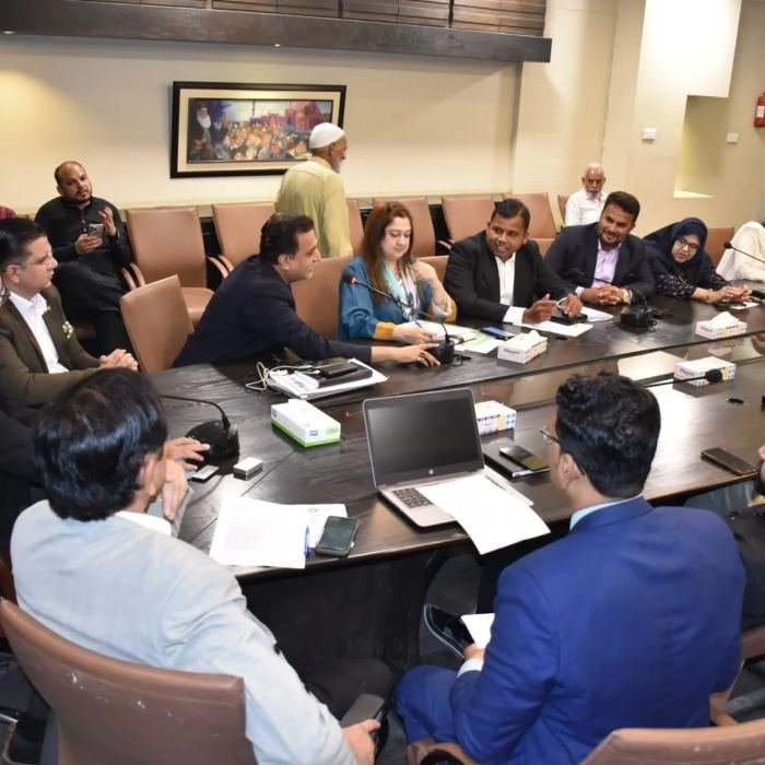 Committee members in discussion around a long meeting table with table microphones and papers