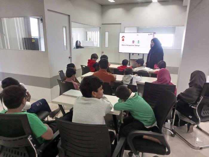 School children seated at tables watching a screen that reads “What is Perspective-Taking?” while a facilitator presents