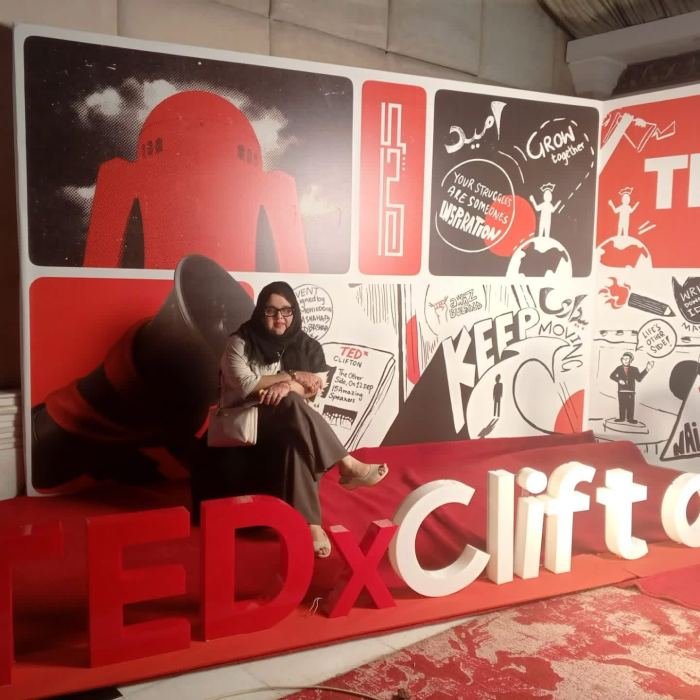 A guest seated in front of illustrated TEDxClifton event signage