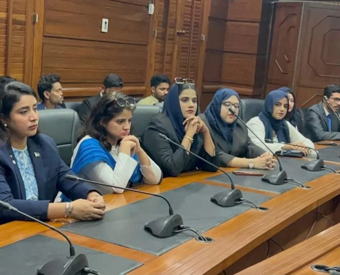 Women delegates seated at desks with microphones in the wood-panelled Sindh Assembly chamber