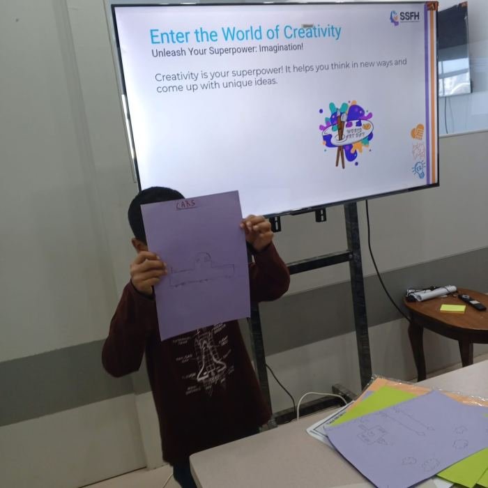 A child holding up his drawing in front of a screen reading “Enter the World of Creativity”